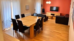 Een eethoek met een houten tafel en stoelen, een televisie en een bank in een kamer met houten vloeren en rode muren.