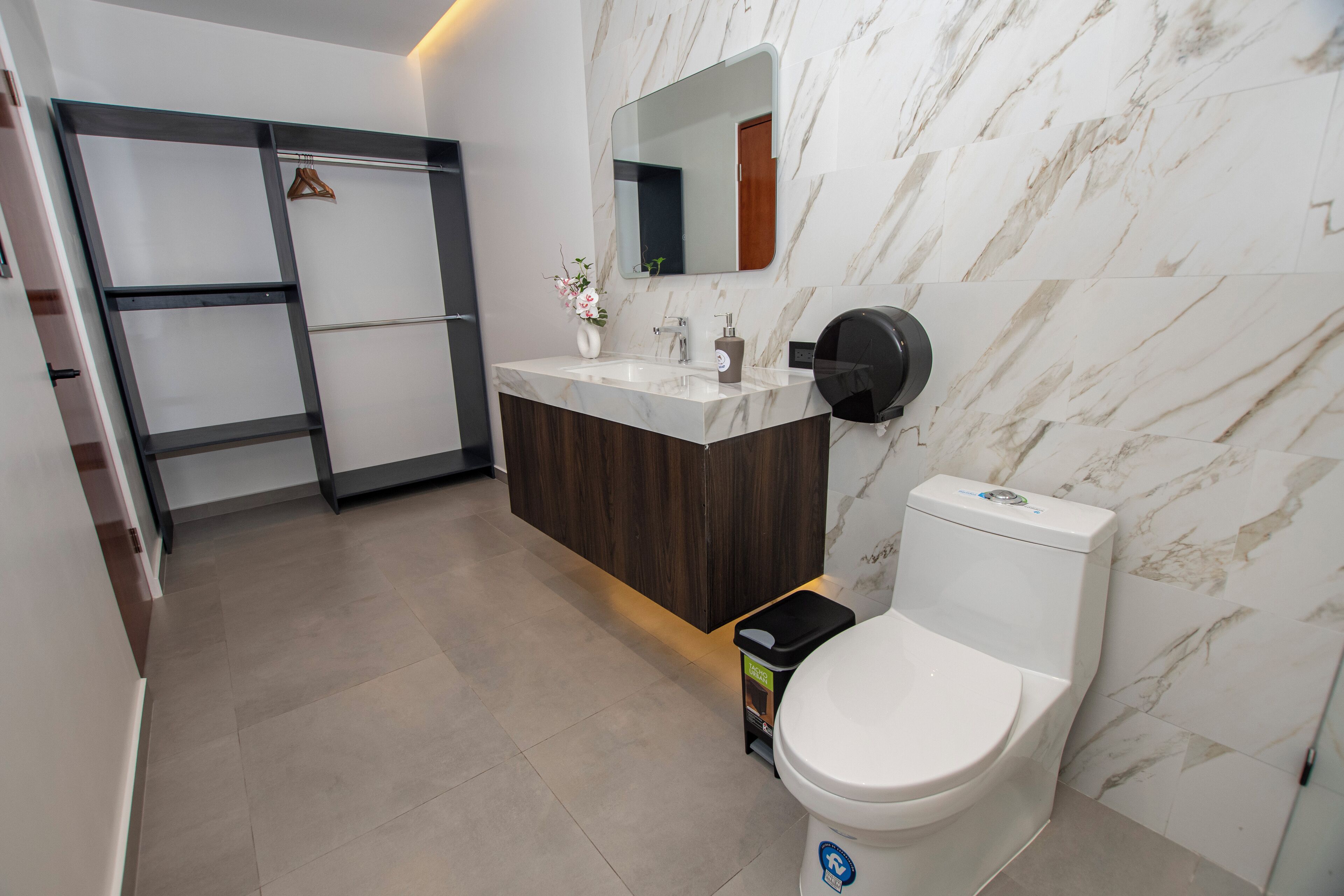 A modern bathroom with a marble wall, a wooden vanity, a toilet, and a shower area.