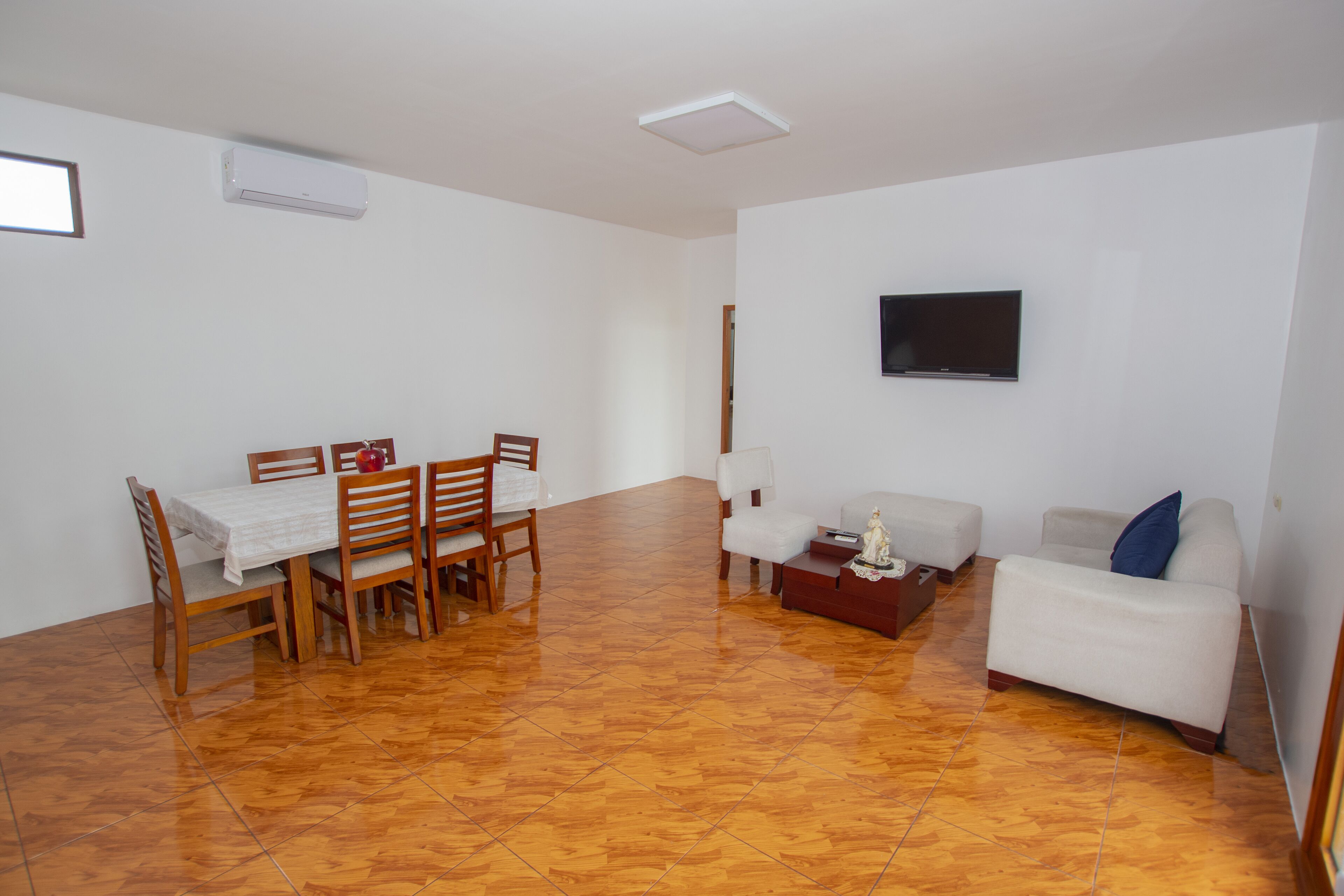 Ein geräumiger Raum mit Esstisch und Stühlen, einer Couch, einem an der Wand befestigten Fernseher und einem Fliesenboden.