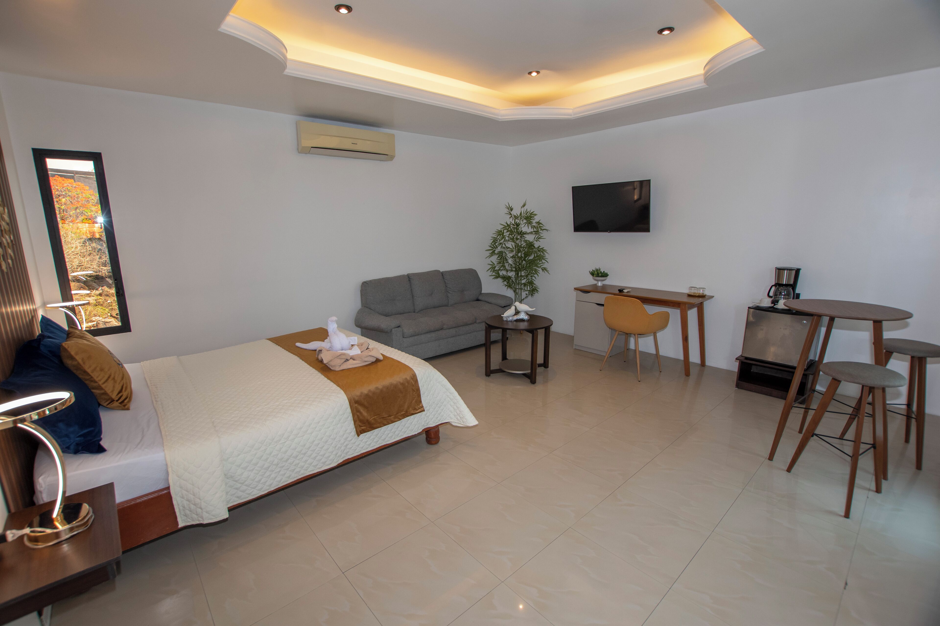 Una habitación de hotel moderna con una cama, un sofá, una mesa de comedor con sillas, un televisor y una planta pequeña.