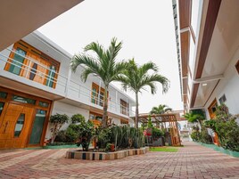 Un patio de hotel con un camino central, palmeras y una zona de estar cubierta.