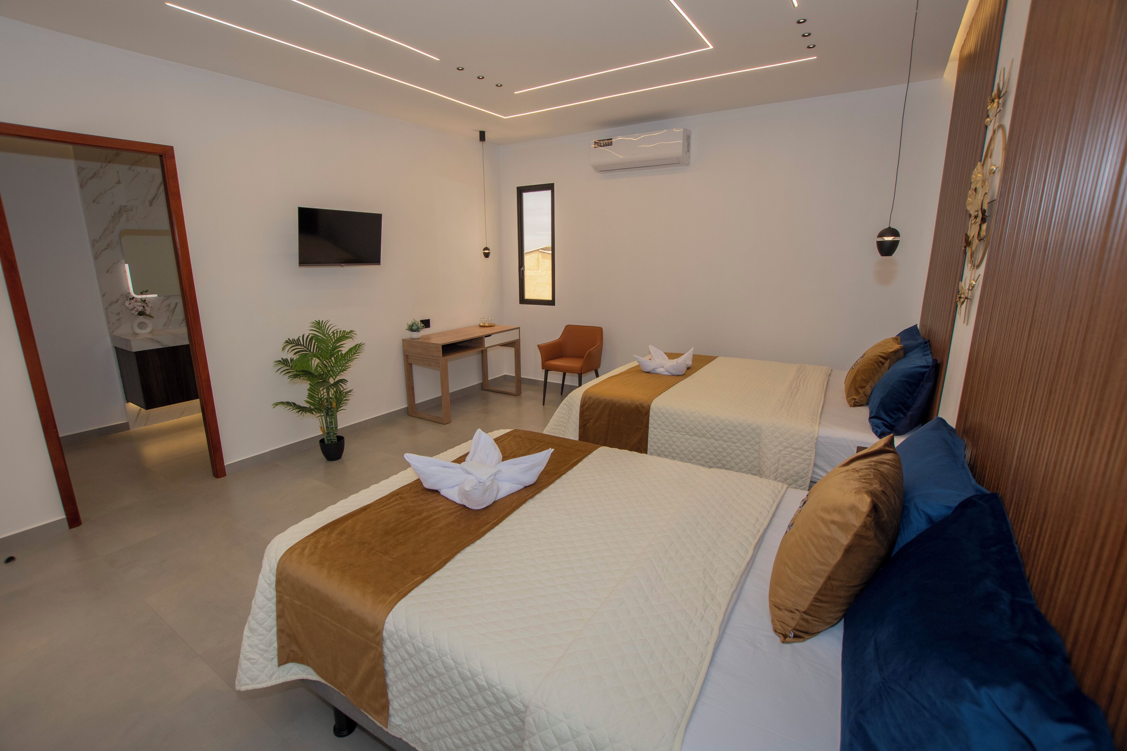 Una habitación de hotel moderna con dos camas, un escritorio, una silla, un televisor y una planta en maceta.