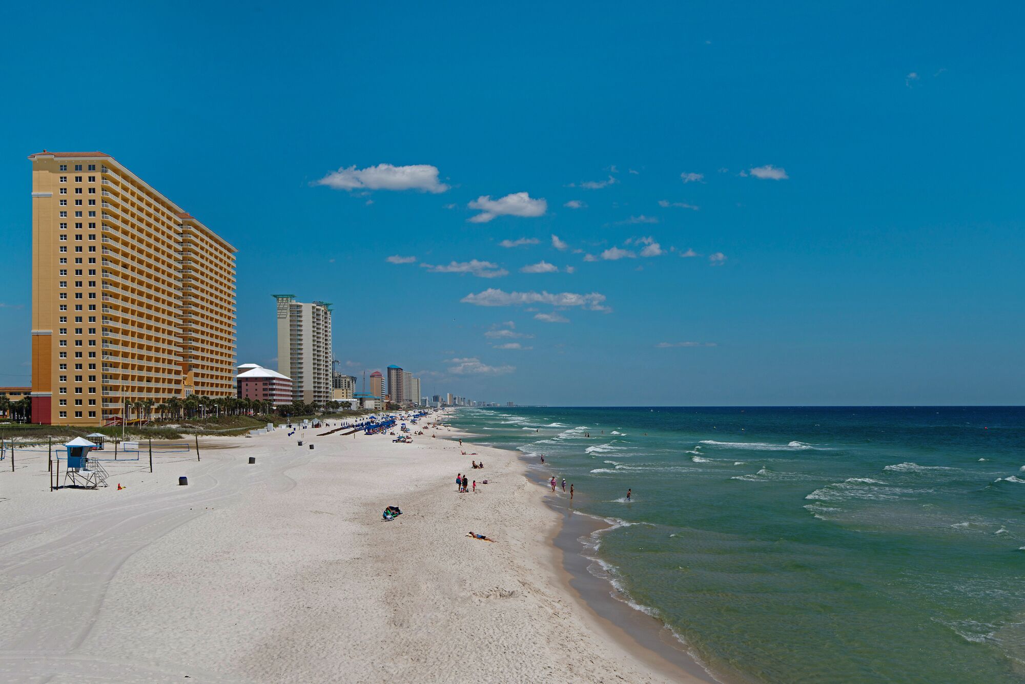 Una playa con un hotel grande a la izquierda, una orilla arenosa y el océano.