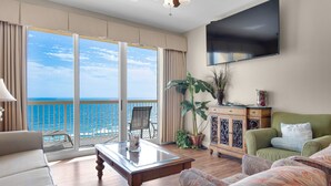 A living room with a large window overlooking the ocean, a flat-screen TV mounted on the wall, and a green sofa. - VIEWS TO BEACHES & RUSSELL-FIELDS PIER!BCH SRVC INCL!! (Panama City Beach)