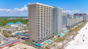A high-rise hotel with multiple balconies, a swimming pool, and a beach view.