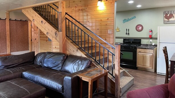 Un salon chaleureux avec un canapé en cuir, un escalier en bois et un coin cuisine.