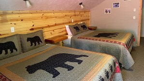 Une chambre confortable avec deux lits, chacun agrémenté d’une courtepointe à motifs d’ours, d’une tête de lit en bois et d’une petite table de chevet.