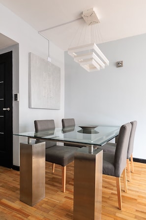 Un espace repas moderne avec une table en verre, des chaises à revêtement gris et un luminaire suspendu.