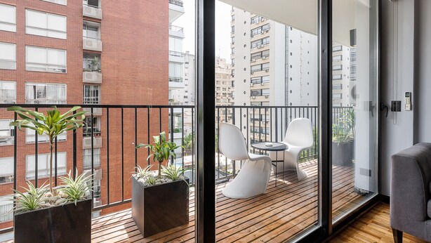 Un balcon doté d’un plancher en bois, de plantes en pot, d’une chaise blanche et d’une petite table.