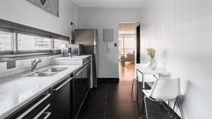 Une cuisine moderne dotée d’appareils électroménagers en acier inoxydable, d’un plan de travail en marbre et offrant une vue sur un coin repas avec une table et des chaises blanches.