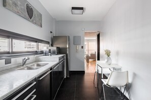 Eine moderne Küche mit Edelstahlgeräten, einer Marmorarbeitsplatte und Blick in einen Essbereich mit weißem Tisch und Stuhl.