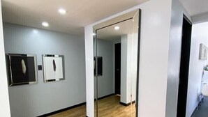 Une pièce spacieuse dotée d’un plancher en bois, d’un grand miroir et de luminaires encastrés dans le plafond.