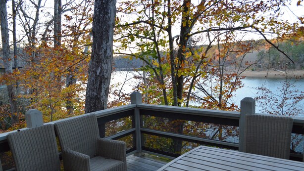A wooden deck with wicker chairs and a table, overlooking a lake with autumn foliage. - Exclusive Smith Lake Slice of Heaven  in the Gated Point William Development.  (Crane Hill)