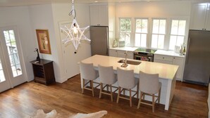 A modern kitchen with white cabinets, a central island with bar stools, a hanging light fixture, and a view of the outdoors through large windows. - Exclusive Smith Lake Slice of Heaven  in the Gated Point William Development.  (Crane Hill)