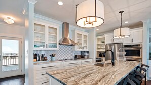 A modern kitchen with white cabinetry, a marble island, stainless steel appliances, and pendant lighting. - Gulf Front Home with 3 Master Bedrooms (Dauphin Island)