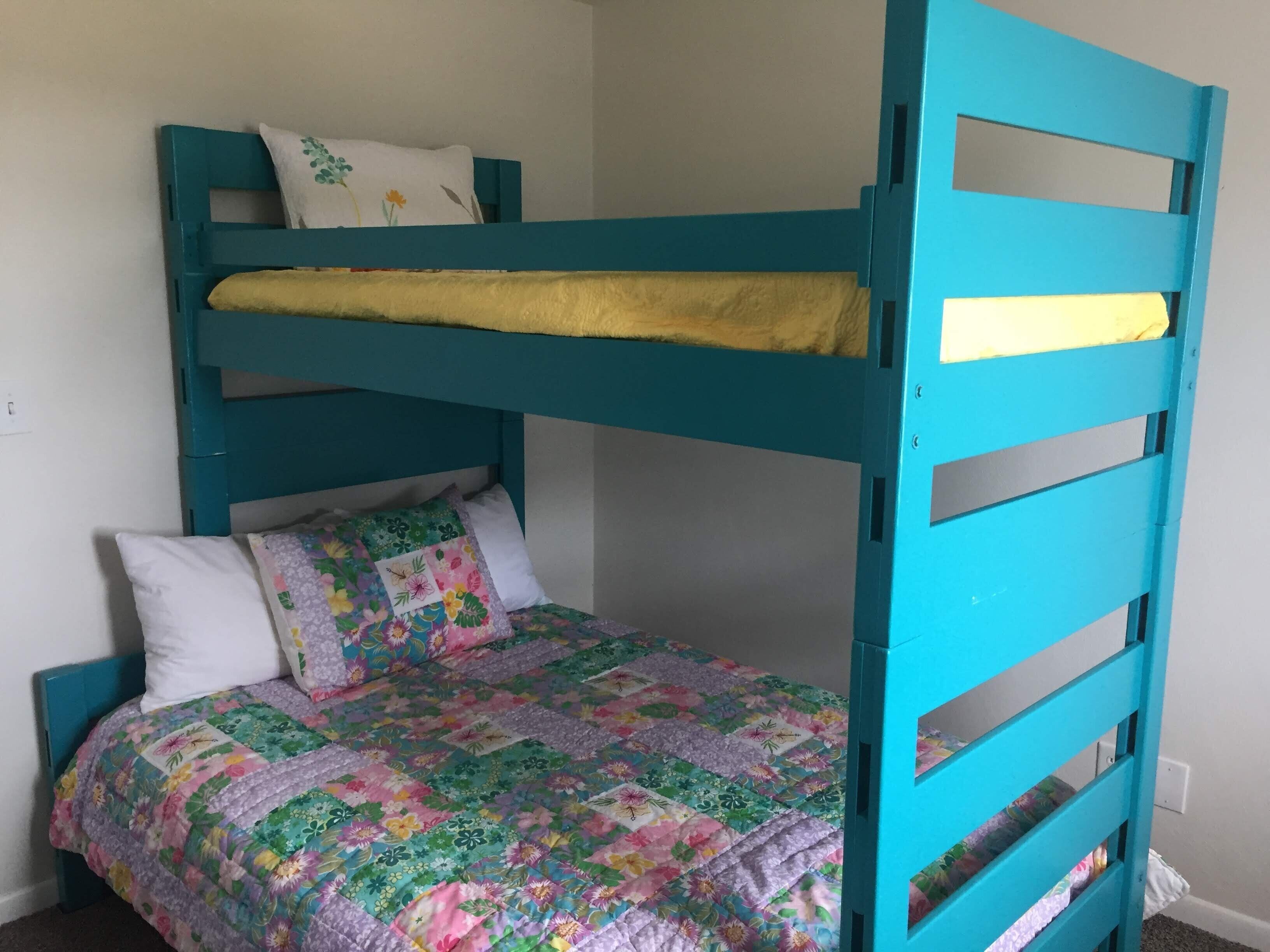 En køjeseng med et farverigt quilt og puder, en hvid væg og en stikkontakt.