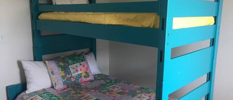 En køjeseng med et farverigt quilt og puder, en hvid væg og en stikkontakt.