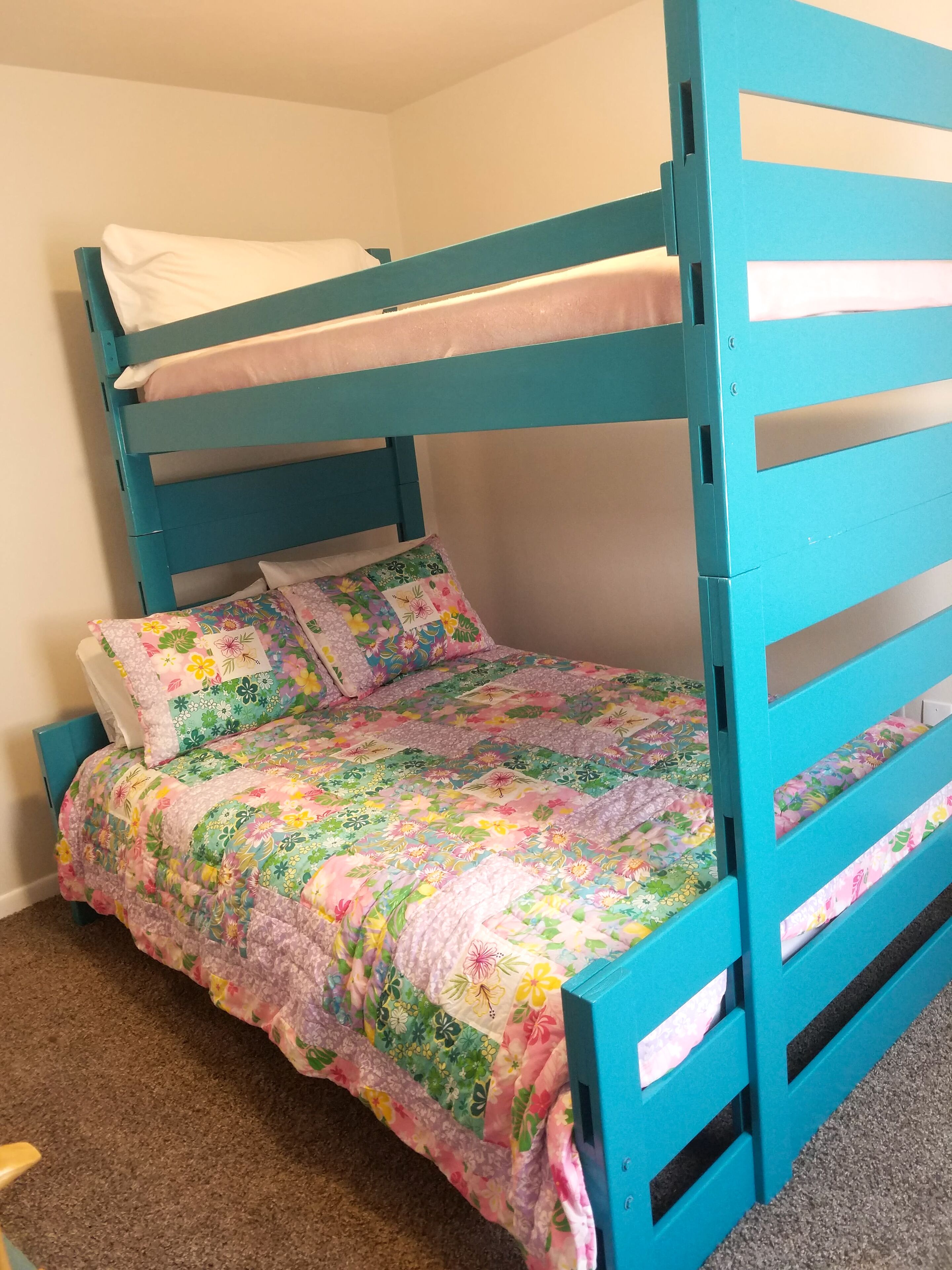 Un lit superposé avec une couette à motifs floraux, un oreiller blanc et une tête de lit bleue.
