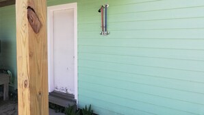 Une façade en bois peinte en vert, avec une porte blanche et un garde-corps en métal.