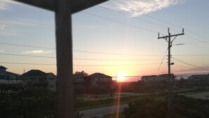 Une vue sur le coucher de soleil depuis un balcon avec une balustrade, des lignes électriques et des maisons en arrière-plan.