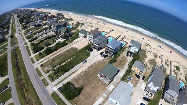 Vue aérienne d’une zone résidentielle côtière, avec des maisons, une plage et une jetée.