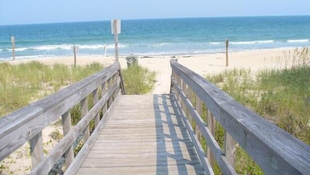 Una passerella in legno che conduce a una spiaggia, con l'oceano sullo sfondo.
