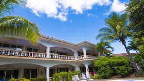 Un edificio de dos pisos con piscina, balcones y jardines tropicales.