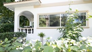 Una casa blanca con balcón, rodeada de abundante vegetación.