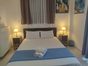 A hotel room with a large bed, two bedside lamps, a blue textured bedspread, and a painting on the wall. - Guest House Kithairon (Mandra-Eidyllia)