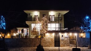 En toetages bygning med en stenfassade, en balkon på øverste etage, og et træ pyntet med lys foran.