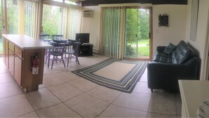 A living room with a sofa, a coffee table, a TV, a dining table with chairs, and a kitchen area with a counter and cabinets. - Berkshire Mountain House (Stephentown)