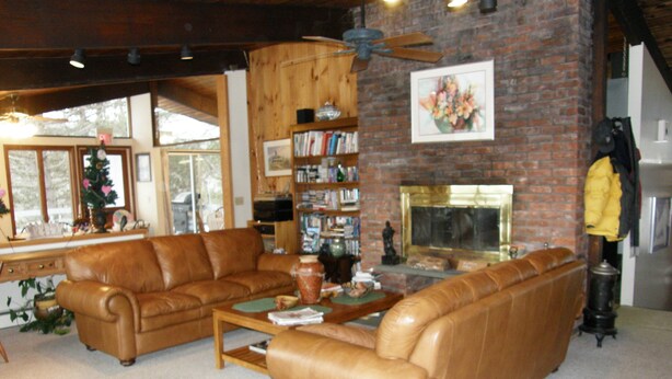 A living room with a fireplace, leather sofas, a coffee table, and a bookshelf. - Berkshire Mountain House (Stephentown)