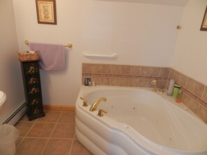 Et badeværelse med et fristående badekar, et toiletbord med blomstermønstret skab og et billede i ramme på væggen.