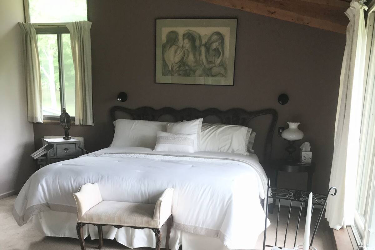Ein Schlafzimmer mit einem großen Bett, einem Sessel, einem Esstisch und einem Bild an der Wand.