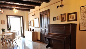 Een ruime kamer met een piano, een eettafel met stoelen en een kamerbreed tapijt.
