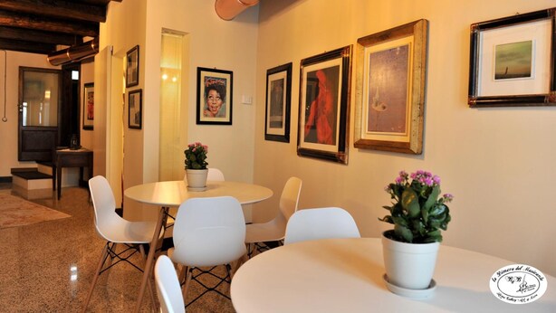 Een eetgedeelte met witte stoelen en tafels, kunstwerken aan de muur en een potplant op tafel.