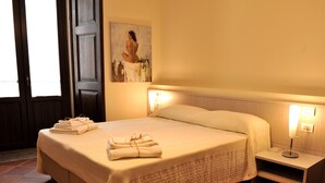 Een hotelkamer met een groot bed, keurig opgevouwen handdoeken, een nachtkastje met een lamp en een schilderij aan de muur.