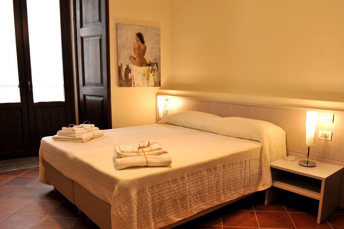 Une chambre d’hôtel avec un grand lit, des serviettes soigneusement pliées, une table de chevet avec une lampe et un tableau au mur.