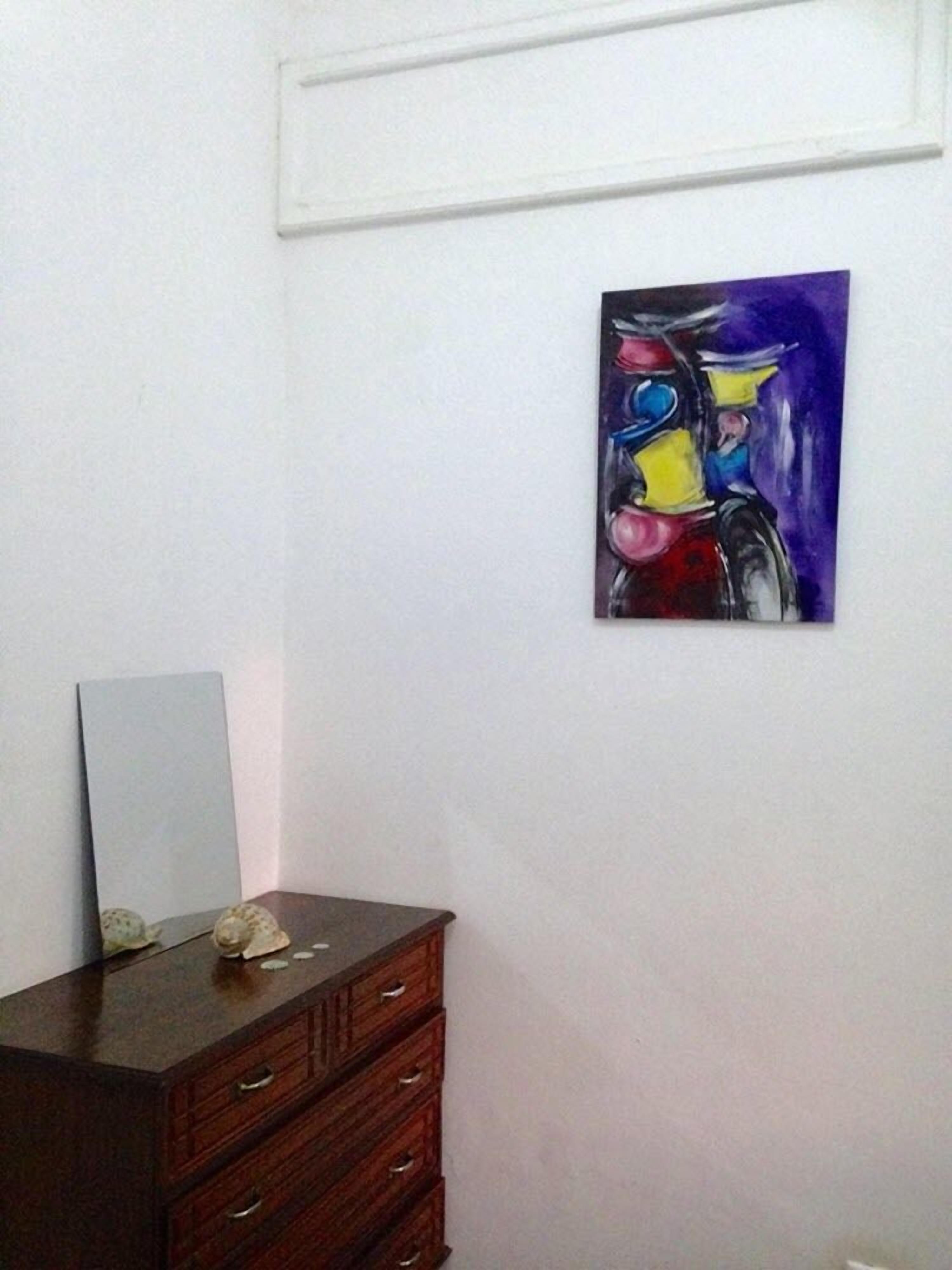 Una habitación con un aparador de madera, un espejo y un cuadro abstracto de colores en la pared.