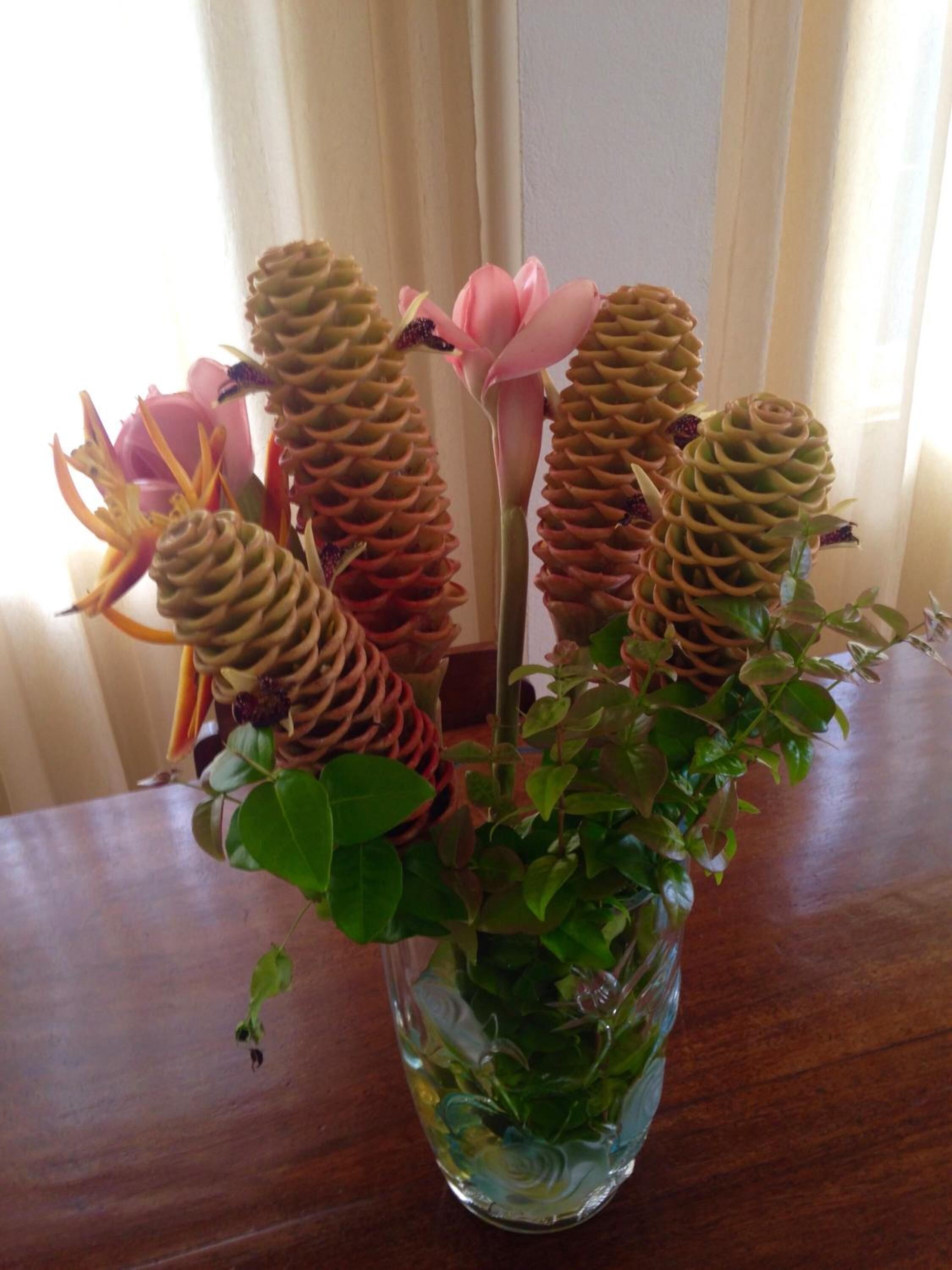 Eine Vase mit grünen Blättern und einer rosa Blüte auf einem Holztisch.