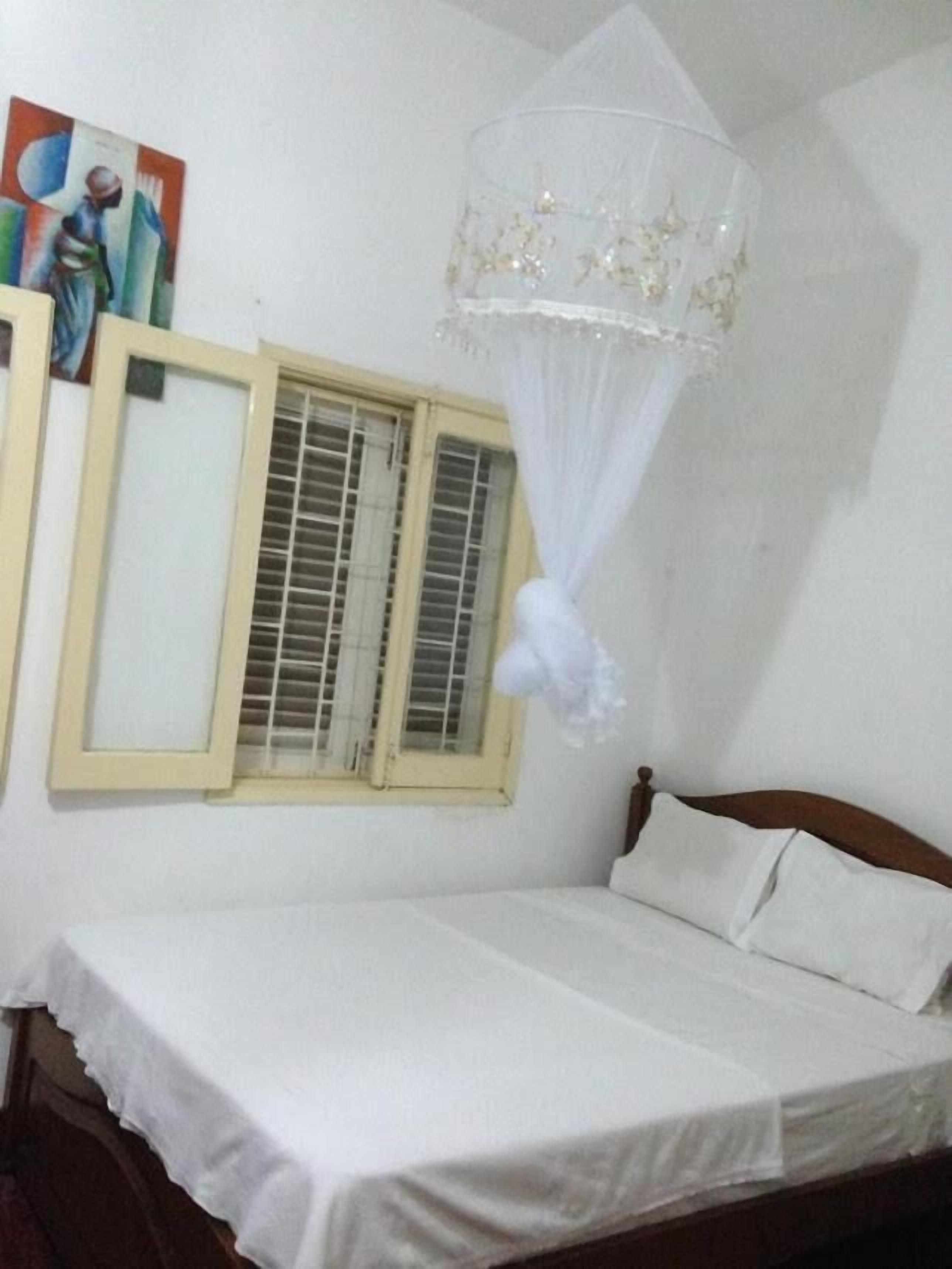 A single bed with a white bedspread, a wooden headboard, and a mosquito net hanging above.
