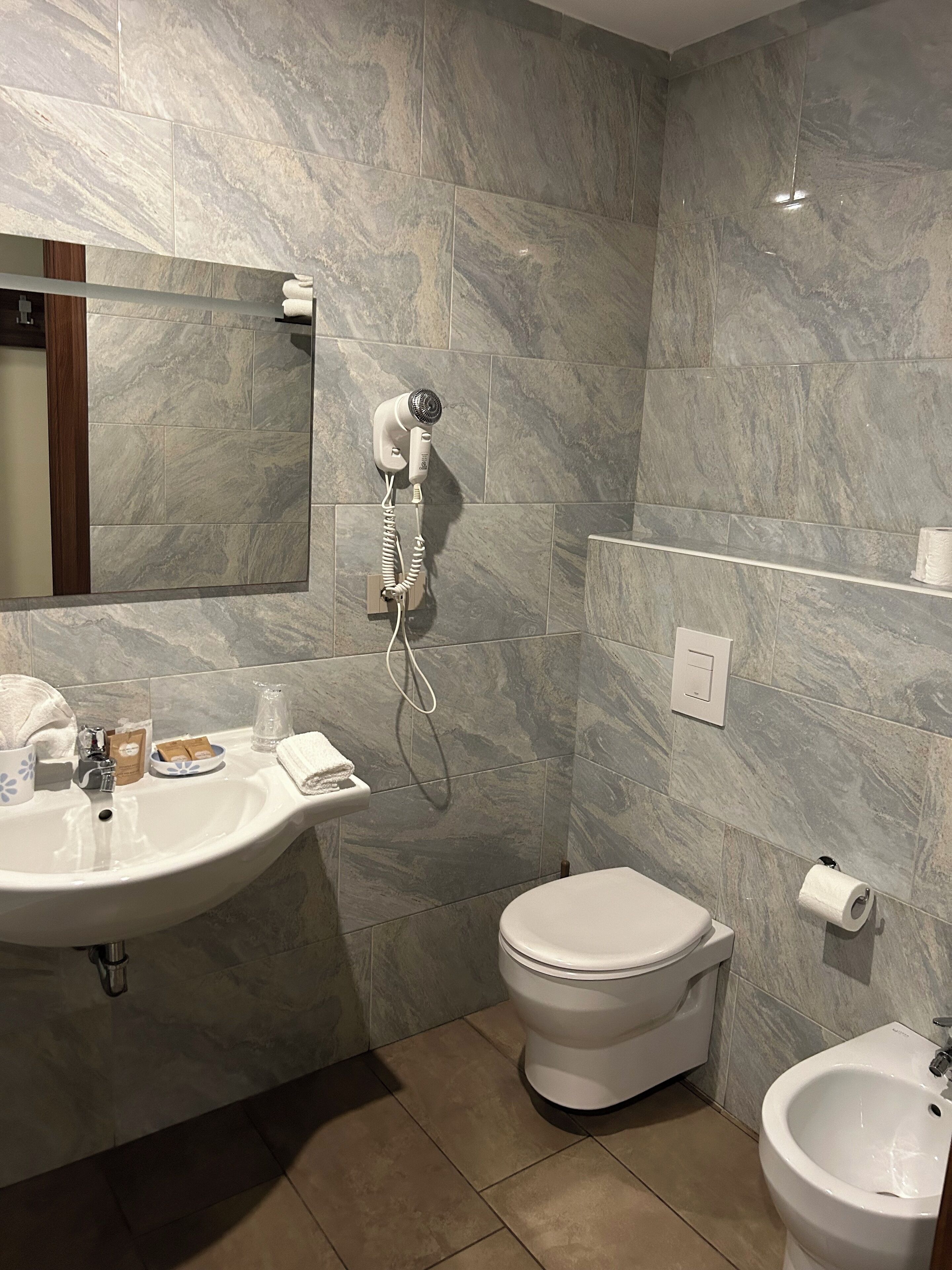 A bathroom with a sink, toilet, bidet, and a hairdryer mounted on the wall.