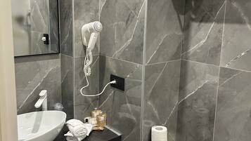 A modern bathroom with a marble backsplash, a white sink, a hairdryer, a towel rack, and a toilet paper holder.