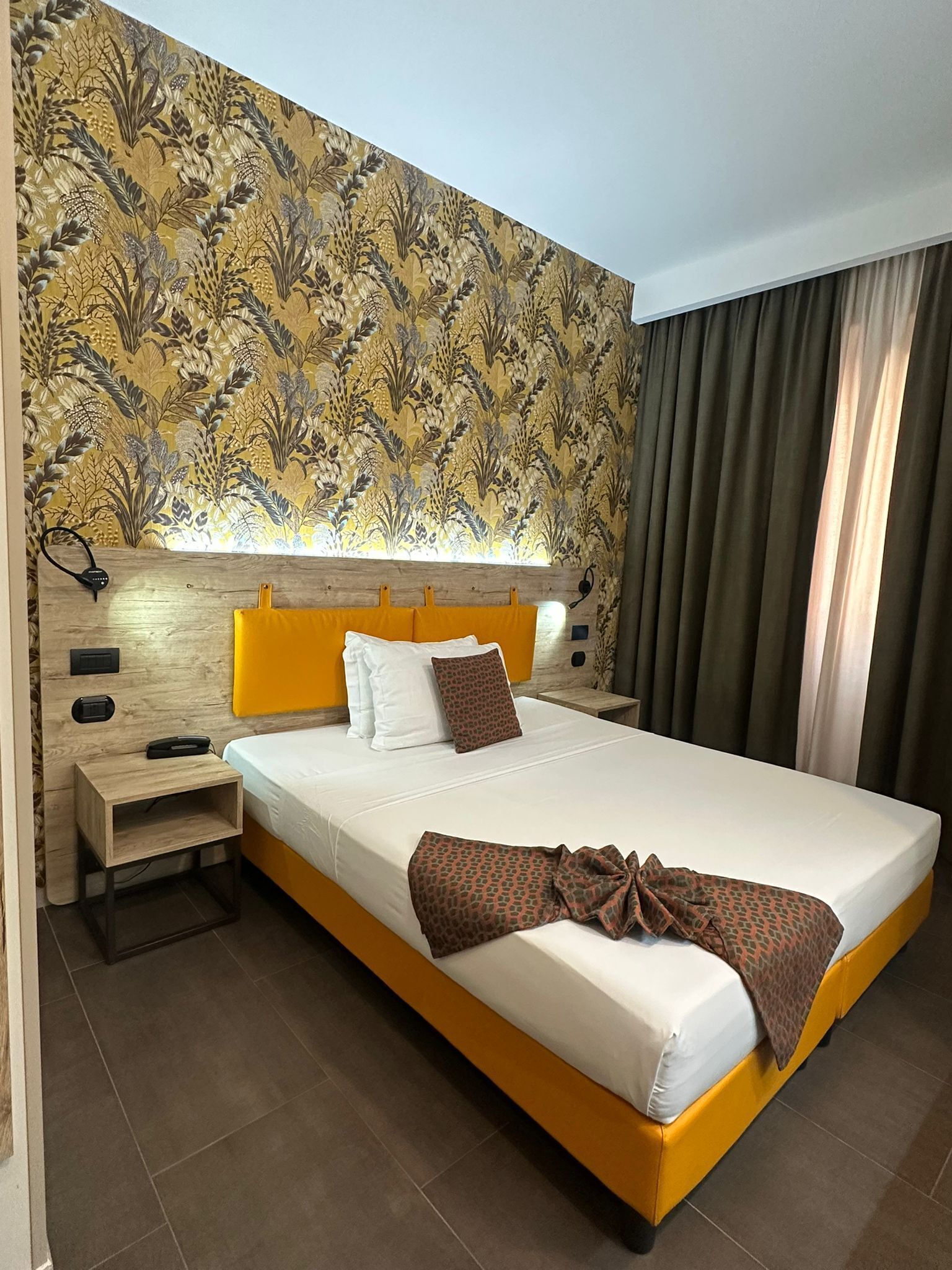 Ein Hotelzimmer mit einem großen Bett, einem Holzkopfende, einem Nachttisch und einer Wand mit Muster.