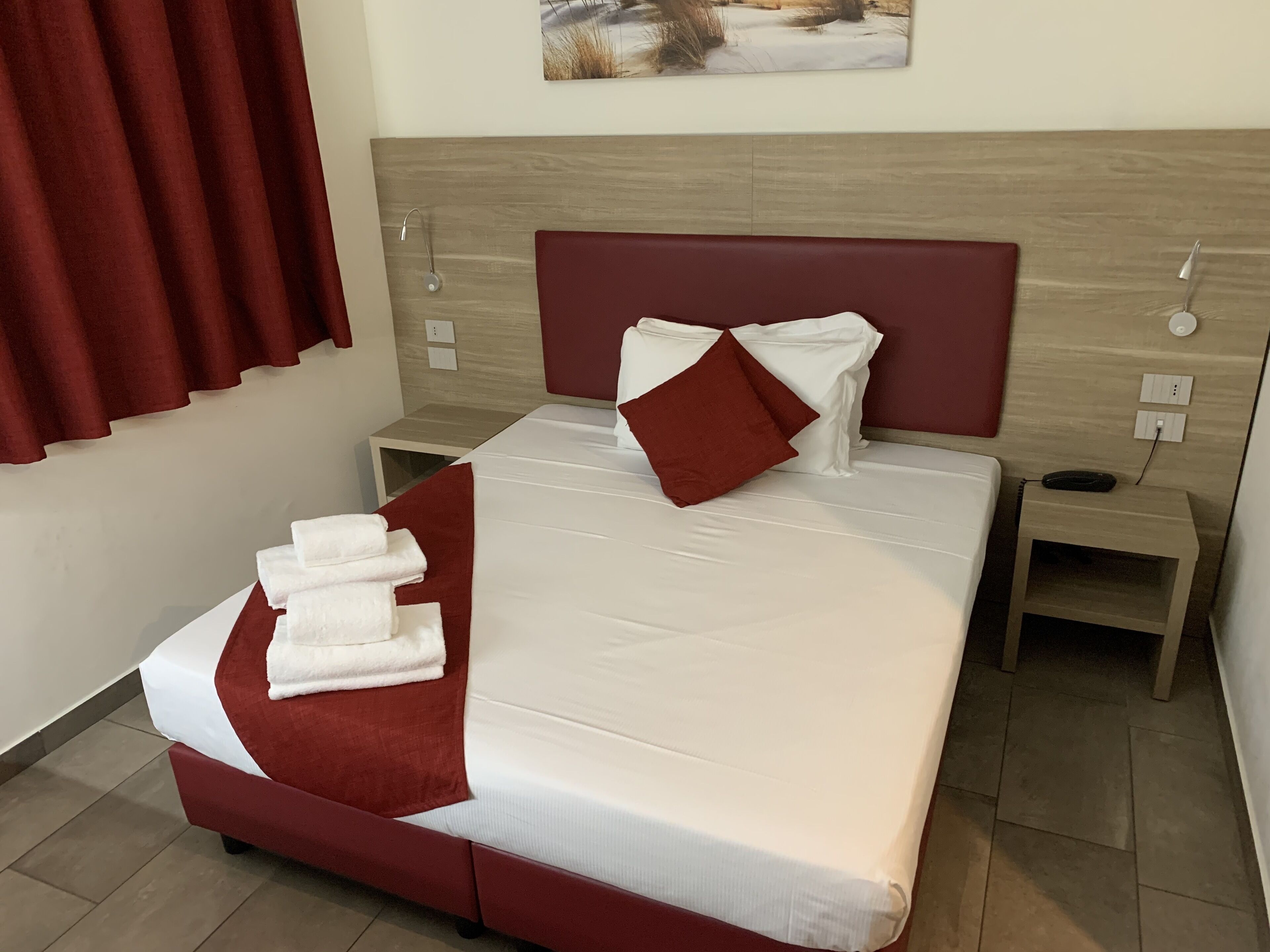 A neatly made bed with white and red bedding, a wooden headboard, and a small bedside table with a phone.