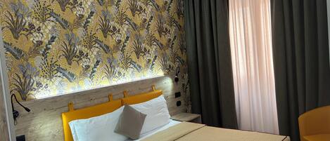 A hotel room with a patterned wallpaper, a bed with a beige cover, a wooden headboard, a bedside table with a phone, and a chair.