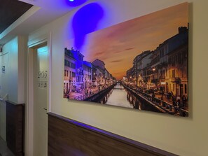 A corridor with a large painting of a sunset over a canal, a door with the number 205, and a blue light fixture on the ceiling.