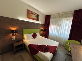 A hotel room with a large bed, two bedside lamps, a nightstand, a green chair, and a painting on the wall.