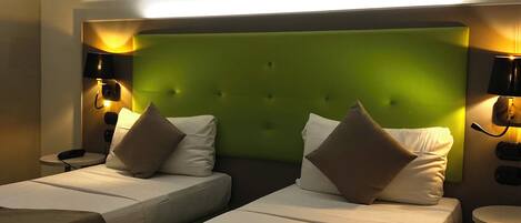 A hotel room with two beds, a green headboard, and a painting of a coastal scene above the beds.