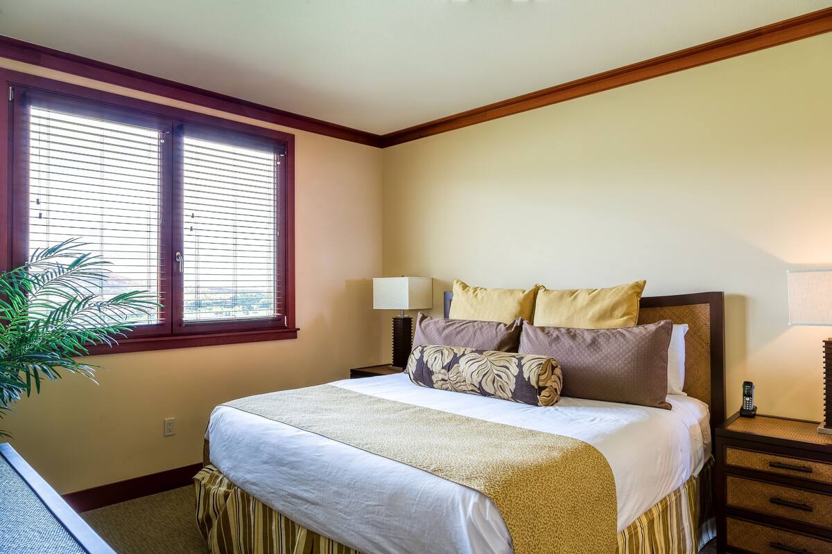 Un dormitorio ordenado con cama, mesitas de noche, lámpara y ventana con persianas.